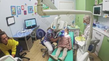 带着一个母亲的孩子在牙医`接待处。 女孩躺在椅子上，在她母亲的身后。 医生和一个